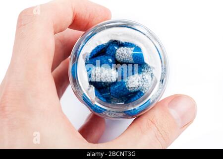 Mann, der in einen Behälter mit offenen Pillen schaut und ihn in der Hand hält, Draufsicht. Blau-weiße, transparente Suplementtabletten mit Granulat in einer Glasflasche Stockfoto