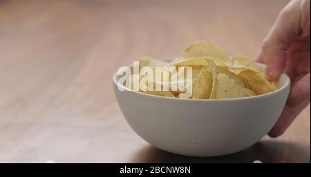 Mann Hand bringen weiße Schüssel mit schwarzem Pfeffer gewürzte Kartoffel Chips auf Nussbaum Holztisch mit Kopierer Platz Stockfoto