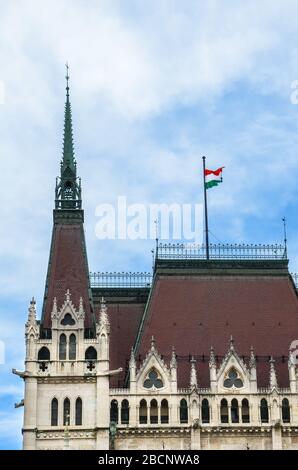 Gebäude des ungarischen Parlaments Orszaghaz in Budapest, Ungarn. Sitz der Nationalversammlung. Haus im neogotischen Stil erbaut. Schwenkende Flagge Ungarns auf dem Haus. Ungarisches Konzept. Stockfoto