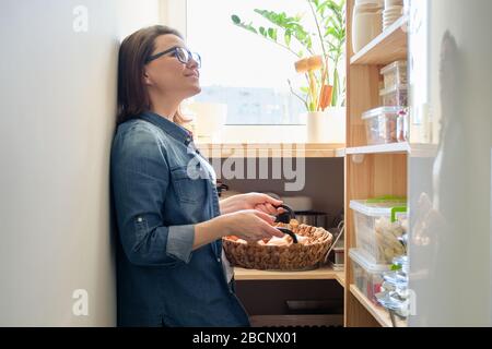 Frau in Pantry, die Korb mit Zwiebeln nimmt, Lebensmittelaufbewahrung in Pantry auf Holzregal Stockfoto