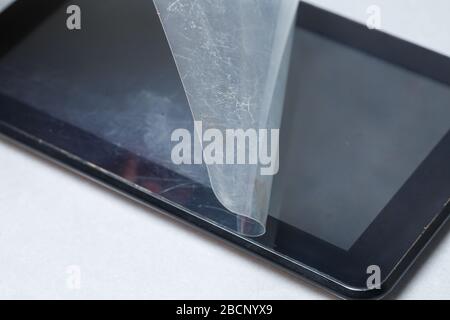 Schwarz verkratztes Tablett mit einer Schutzfolie auf grauem Hintergrund. Schützen Sie den Bildschirm Ihres Geräts Stockfoto