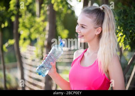 Frau macht eine Pause vom Sport und trinkt aus ihrer Wasserflasche Stockfoto