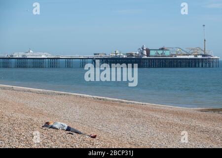 Ein paar Leute sitzen oder gehen an einem leeren Brighton Beach entlang während der Corona Virus Lockdown trotz des heißen Frühlings Tag. Die Polizei erzwang soziale Distanzierung. Stockfoto