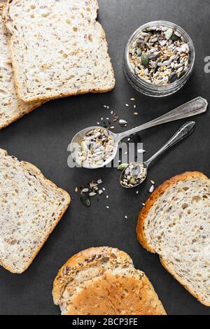 Gesunde Brotscheiben auf dunklem Hintergrund mit einer Mischung aus Samen, Draufsicht. Stockfoto