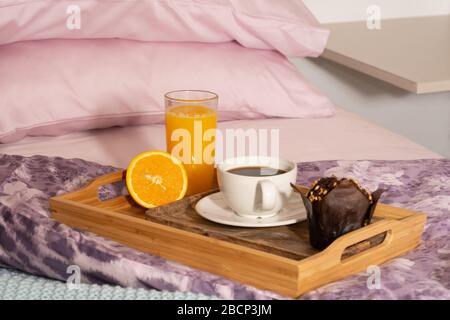 Frühstück im Bett mit Muffin, Orangensaft und Kaffee. Bett in violetten Tönen. Stockfoto