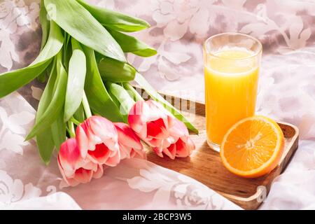 Gesunder Orangensaft im Bett auf einem Holztablett und weiß-rosa Bouquet von frisch geschnittenen Tulpen Stockfoto