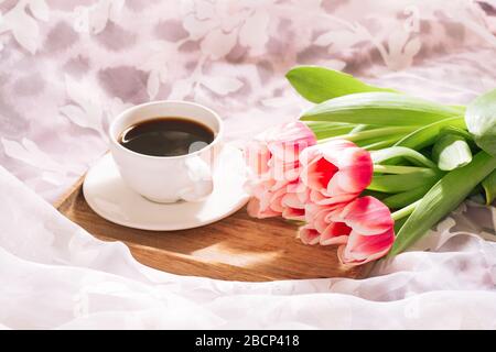 Eine Tasse duftenden frisch gemahlenen Kaffee mit einem frischen Bouquet von weiß-rosa Tulpen auf einem Holztablett Stockfoto