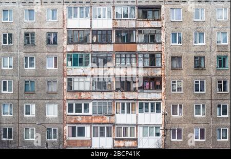 Fassade eines grauen, mehrstöckigen sowjetischen Plattenbaus. Russische alte städtische Wohnhäuser mit Fenstern. Typisch russische Nachbarschaft. Stockfoto