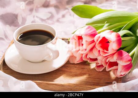 Eine Tasse duftenden frisch gemahlenen Kaffee mit einem frischen Bouquet von weiß-rosa Tulpen auf einem Holztablett Stockfoto