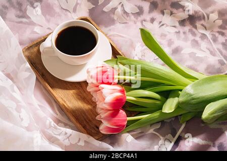 Eine Tasse duftenden frisch gemahlenen Kaffee mit einem frischen Bouquet von weiß-rosa Tulpen auf einem Holztablett Stockfoto