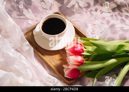 Eine Tasse duftenden frisch gemahlenen Kaffee mit einem frischen Bouquet von weiß-rosa Tulpen auf einem Holztablett Stockfoto