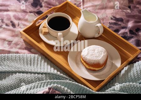 Frühstück in einem gemütlichen Bett mit frisch gebrühtem, schmackhaftem und duftendem Kaffee, Rohrzucker, frischer Milch und leckeren Donut in Puderzucker gegen ein Stockfoto