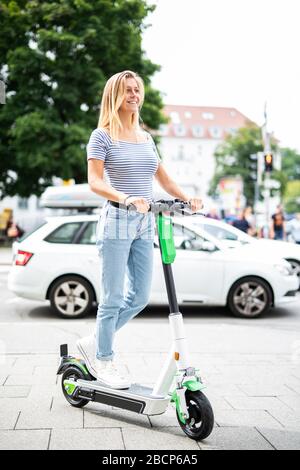 Hübsche junge Frau ist in der Stadt mit einem Elektroroller unterwegs Stockfoto