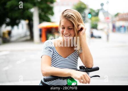 Hübsche junge Frau ist in der Stadt mit einem Elektroroller unterwegs Stockfoto