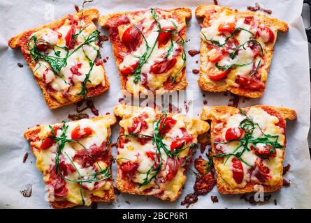 Gebackene Sandwiches mit Mozzarella-Käse, Wurst, Tomaten und Rucola auf Papier Draufsicht Stockfoto