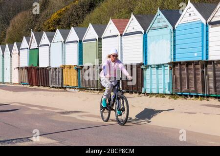 Bournemouth, Dorset, Großbritannien. April 2020. UK Wetter: Warm sonnigen Tag, wie die Menschen gehen an die Küste, um ihre tägliche Übung, die meisten halten sich an die Coronavirus Einschränkungen für soziale Distancing. Junge Frau Radfahren entlang der Promenade vorbei an Strandhütten - Fahrrad Fahrrad Fahrrad Radfahrer. Quelle: Carolyn Jenkins/Alamy Live News Stockfoto