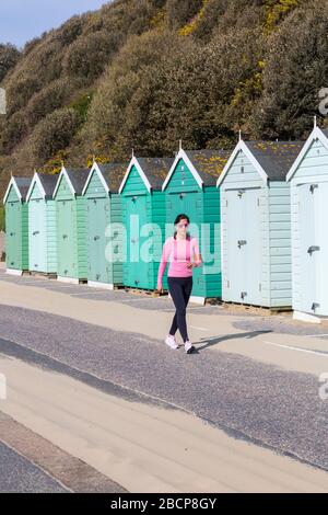 Bournemouth, Dorset UK. April 2020. Wetter in Großbritannien: Sonniger Tag, an dem die Menschen am Meer ihre tägliche Bewegung Unternehmen, am meisten unter Einhaltung der Einschränkungen von Coronavirus für soziale Distanzierungen. Junge Frau, die an der Promenade vorbei an Strandhütten spazieren geht. Credit: Carolyn Jenkins/Alamy Live News Stockfoto