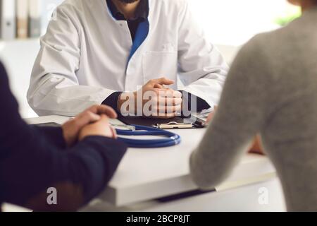 Selbstbewusster Arzt und paarter Patient sitzen am Tisch in der Klinik. Hausarzt. Stockfoto