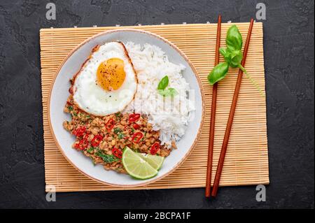 Pad Krapow Gai - thailändisches Basil Chicken mit Reis und gebratenem Ei schwarzer Schieferhintergrund. Pad Krapow ist ein thailändisches Gericht mit Hackhuhn oder Schweinefleisch, Stockfoto