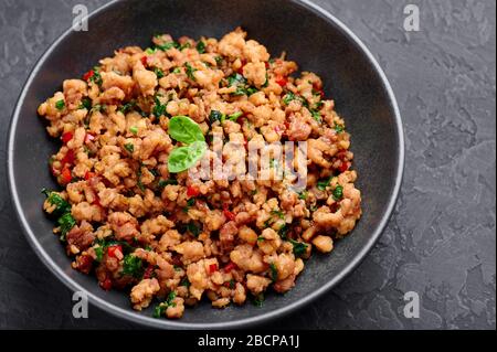 Pad Krapow Gai - Thai-Basil-Huhn in schwarzer Schüssel mit dunklem Schieferhintergrund. Pad Krapow ist ein thailändisches Gericht mit Hackhuhn oder Schweinefleisch, Basilikum, s. Stockfoto