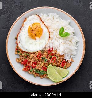 Pad Krapow Gai - thailändisches Basil Chicken mit Reis und gebratenem Ei schwarzer Schieferhintergrund. Pad Krapow ist ein thailändisches Gericht mit Hackhuhn oder Schweinefleisch, Stockfoto