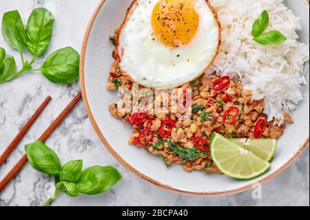 Pad Krapow Gai - Thai-Basil-Huhn mit Reis und gebratenem Ei auf weißem Marmorhintergrund. Pad Krapow ist ein thailändisches Gericht mit Hackhuhn oder Schweinefleisch Stockfoto