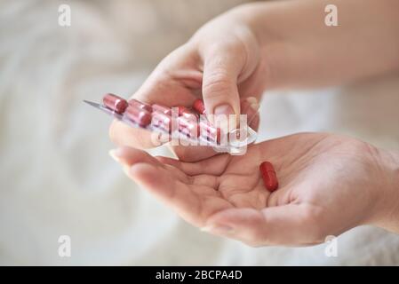 Nahaufnahme der Hände einer kranken jungen Frau. Mädchen im Bett, die Blister und Tabletten oder Pillen hält. Painkiller mit Platz für Text. Verschwommener Hintergrund Stockfoto