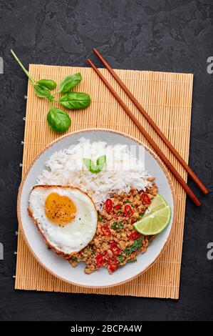 Pad Krapow Gai - thailändisches Basil Chicken mit Reis und gebratenem Ei schwarzer Schieferhintergrund. Pad Krapow ist ein thailändisches Gericht mit Hackhuhn oder Schweinefleisch, Stockfoto