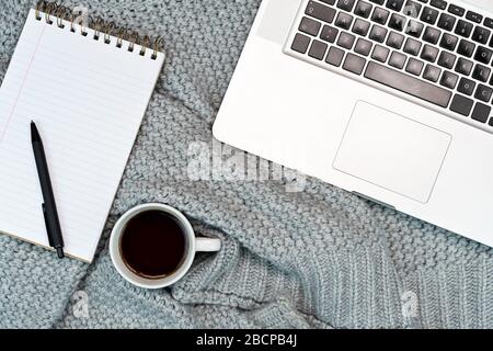 Gemütlicher Schreibplatz mit warmem Pullover, Kaffee, Laptop und Schreibzubehör. Arbeiten Sie von zu Hause aus. Schreiben. Warmes Konzept bei kaltem Wetter. Stockfoto