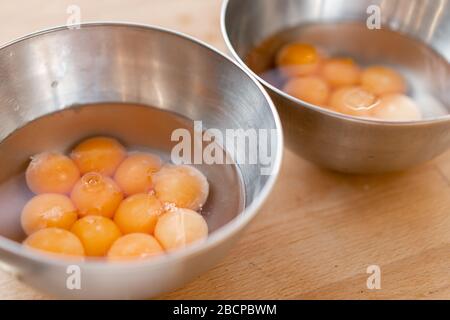 Zwei Edelstahl Schüsseln mit viele gesprungene Eier mit Eigelb gefüllt, in den hölzernen Tisch. Close Up. Stockfoto