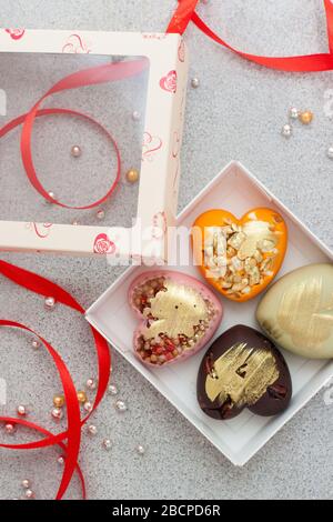 Geschenkbox mit herzförmiger farbiger Schokolade, verziert mit rotem Band. Steingrauer Hintergrund. Viel Kopierspeicher. Stockfoto