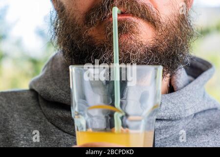 Bärtiger Mann im Kapuzenpullover, der Saft mit Stroh trinkt Stockfoto