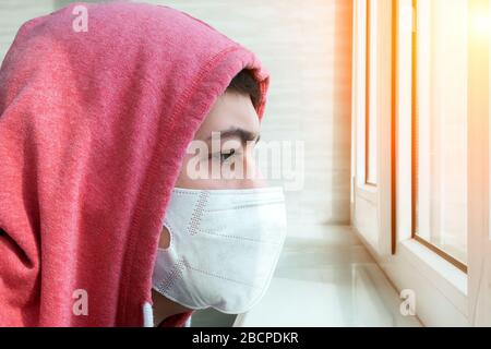 Mann in einer Schutzmaske zu Hause, während er sich selbst isoliert und unter Quarantäne stellt, trägt er eine chirurgische medizinische Maske, um sein Gesicht vor dem er schützt Stockfoto