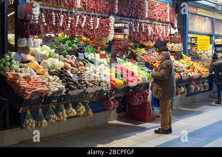 Ein Mann schaut sich im Winter auf einem Marktstand für frisches Gemüse in der Central Market Hall, Budapest, Ungarn, Produkte an Stockfoto