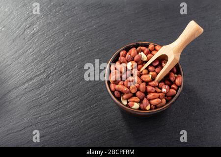 Ungesellte Erdnüsse in einer Tonschale auf einem schwarzen Brett. Ansicht von oben. Platz für Text. Stockfoto