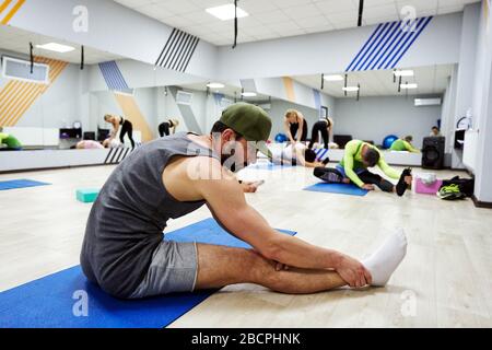 Echtes Training einer Gruppe von Menschen in einem Fitness-Center. Der Mann im Vordergrund macht Dehnübungen. Stockfoto