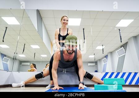 Echtes Training einer Gruppe von Menschen in einem Fitness-Center. Der Lehrer hilft dem Mann, Dehnübungen zu machen. Stockfoto