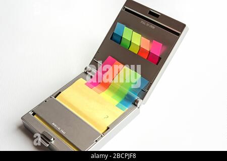 Silberfarbener Spender aus gelben postit-Notizen und mehrfarbigen Haftmarkenmarkenhoch vor weißem Hintergrund, Fragezeichen auf postit-Note geschrieben. Stockfoto