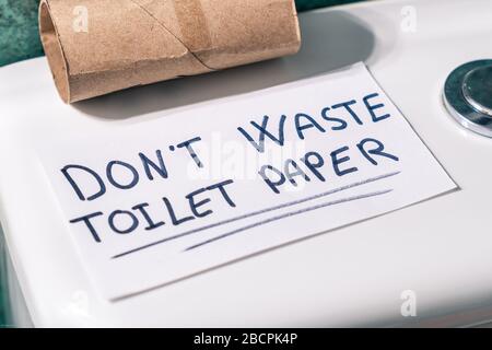 Verschwenden Sie nicht das Toilettenpapier. Nachricht auf einem Papier mit einer fertigen Rolle Toilettenpapier wegen Coronavirus geschrieben. Stockfoto