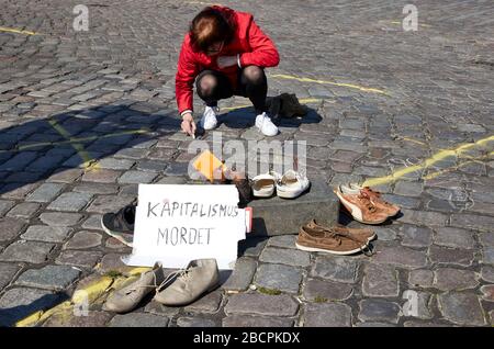 Hamburg, Deutschland. April 2020. Eine Frau zieht die Umrisse ihres Schuhs mit Kreide auf den Pflaster am St. Pauli Fischmarkt. Im Vordergrund steht ein Karton mit der Aufschrift: "Kapitalismus-Morde" und Paar Schuhe ausgestellt. Ein bundesweiter Aktionstag von "Seebrücke Hamburg" und "Freitag für die Zukunft" unter dem Motto "#LeaveNoOneBeid" fordert sowohl die Räumung der Lager als auch die Eröffnung der leerstehenden Hotels zur Unterbringung von Obdachlosen und Flüchtlingen. Credit: Dpa / Alamy Live News Stockfoto