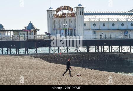 Brighton UK 5. April 2020 - EIN Wanderer mit seinem Hund an einem ruhigen Brighton Strand an einem warmen sonnigen Tag mit Temperaturen, die während der Coronavirus COVID-19-Pandemiekrise in London zwanzig Grad erreichen werden. Gesundheitsminister Matt Hancock hat heute gesagt, dass sie die Regeln für die Ausübung möglicherweise überarbeiten müssen, da zu viele Menschen die Richtlinien ignorieren. Kredit: Simon Dack / Alamy Live News Stockfoto