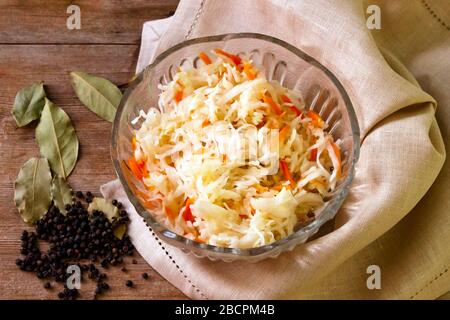 Hausgemachtes fermentiertes Sauerkraut in Glasschale auf rustikalem Holzhintergrund, LeinenServiette, Paprika, Lorbeerblätter Stockfoto