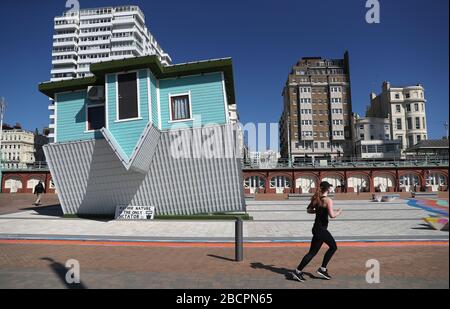 Ein Jogger läuft am kopfüber liegenden Haus an der Brighton Meeresfront vorbei, da Großbritannien weiterhin in Sperrstellung bleibt, um die Ausbreitung des Coronavirus einzudämmen. Stockfoto