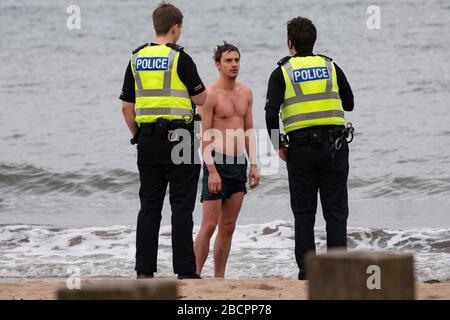 Portobello, Edinburgh, Schottland, Großbritannien. April 2020. Am zweiten Sonntag des Coronavirus Sperrens in Großbritannien nimmt die Öffentlichkeit ihre tägliche Übung nicht ab. Abgebildet. Die Polizei spricht mit dem Mann in Badehosen am Strand von Portobello. Nach der Diskussion durfte der Mann weiter schwimmen. Iain Masterton/Alamy Live News Stockfoto