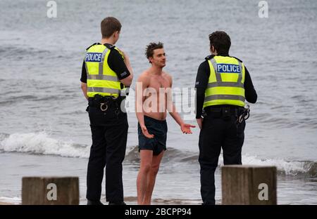 Portobello, Edinburgh, Schottland, Großbritannien. April 2020. Am zweiten Sonntag des Coronavirus Sperrens in Großbritannien nimmt die Öffentlichkeit ihre tägliche Übung nicht ab. Abgebildet. Die Polizei spricht mit dem Mann in Badehosen am Strand von Portobello. Nach der Diskussion durfte der Mann weiter schwimmen. Iain Masterton/Alamy Live News Stockfoto