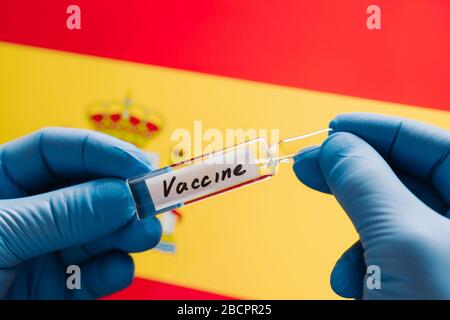 Kampf gegen Coronavirus. Mediziner entwickelt Impfstoff für Covid-19. Hände in medizinischen Handschuhen mit Impfstoff vor Spanien Flagge Hintergrund. Gesundheit ca. Stockfoto