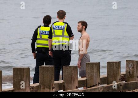 Portobello, Edinburgh, Schottland, Großbritannien. April 2020. Am zweiten Sonntag des Coronavirus Sperrens in Großbritannien nimmt die Öffentlichkeit ihre tägliche Übung nicht ab. Abgebildet. Die Polizei spricht mit dem Mann in Badehosen am Strand von Portobello. Nach der Diskussion durfte der Mann weiter schwimmen. Iain Masterton/Alamy Live News Stockfoto