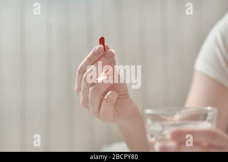 Nahaufnahme der Hände junger Frau. Mädchen im Bett, das Tabletten oder Pillen und Glas Wasser hält. Painkiller mit Platz für Text. Verschwommener Hintergrund. Stockfoto