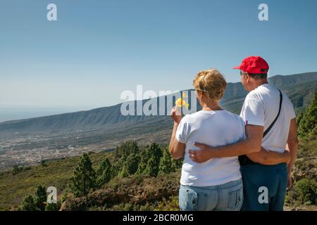 Ältere kaukasische Paar Blick auf die grünen Hänge des Guimar-Tal in einer romantischen Umarmung, aus dem Blickwinkel als Mirador de Chivisaya, Teneriffa bekannt Stockfoto