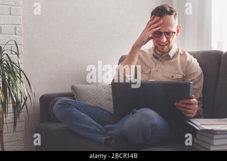 Alarmierter Mann am Computer zu Hause. Liest Nachrichten, arbeitet. Stockfoto